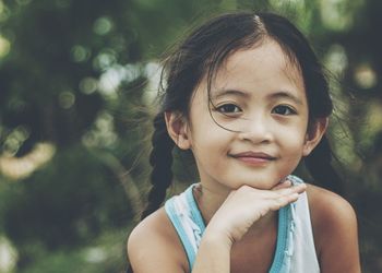 Close-up portrait of smiling girl with hand on chin sitting at park