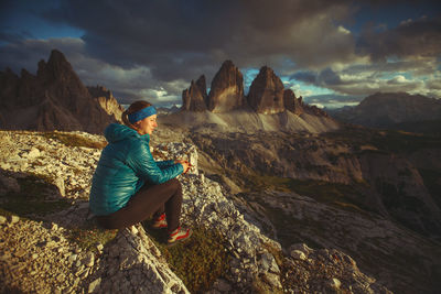 Woman sitting on rock looking at mountains against sky