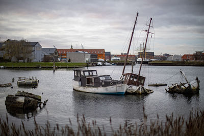 Fishing boats moored at harbor against sky