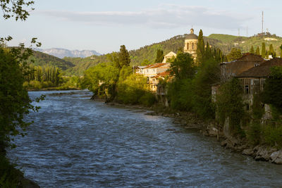 River amidst buildings and trees against sky