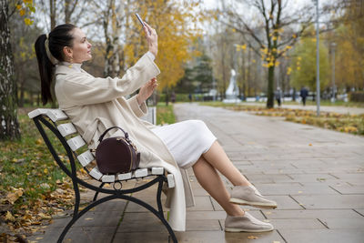 Woman taking selfie while sitting on bench at street
