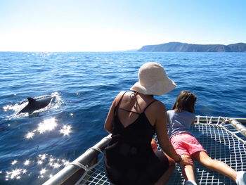 Rear view of woman and daughter sitting in boat in sea