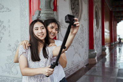 Smiling women embracing while vlogging in corridor