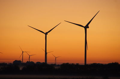 Silhouette wind turbines on field against orange sky