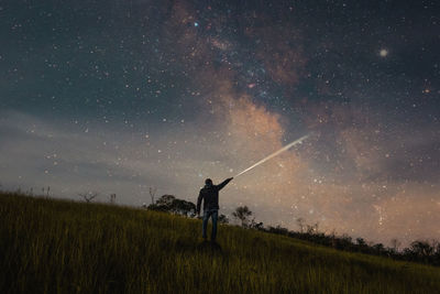 Rear view of man holding flashlight on land against star field