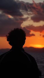 Rear view of man standing by sea against sky during sunset