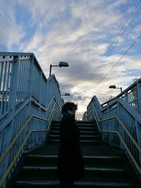 Side view of woman standing on steps against cloudy sky