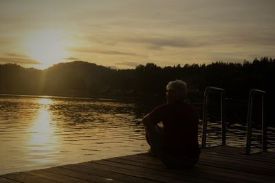 Rear view of man sitting on pier at sunset