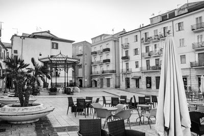 Empty chairs and tables at sidewalk cafe against buildings in city