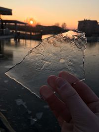 Close-up of hand holding ice crystals against sky during sunset