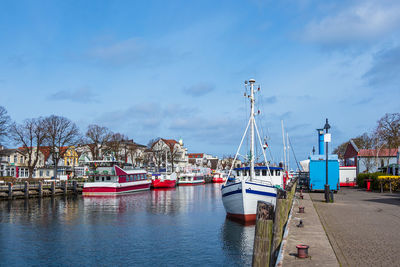 Sailboats moored at harbor against sky in city