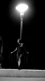 Low angle view of man standing on illuminated street light at night