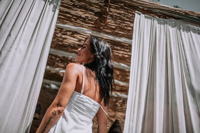 Woman looking at camera while standing against curtain