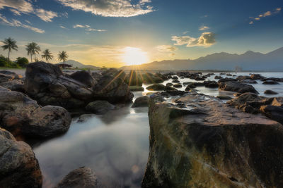 Rocks in sea against sky during sunset
