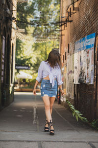 Young woman holding twig while walking on alley