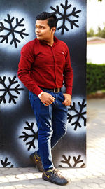 Young man looking away while standing against wall