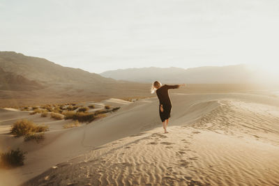 Rear view of woman walking at desert against sky during sunset