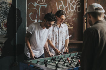 Friends playing foosball against graffiti wall at club