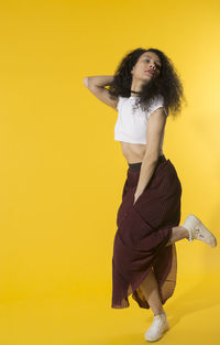 Young woman looking away while standing against yellow background