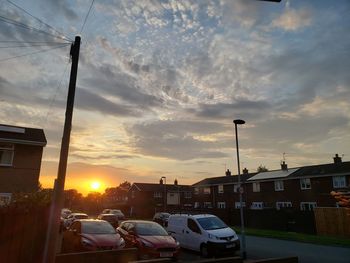 Cars on street by buildings against sky during sunset