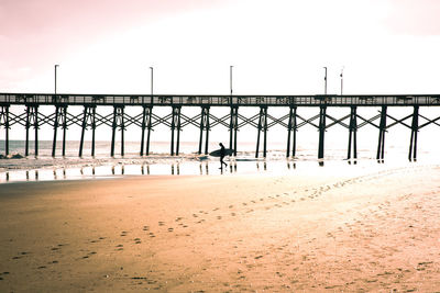 Pier on beach against sky during sunset