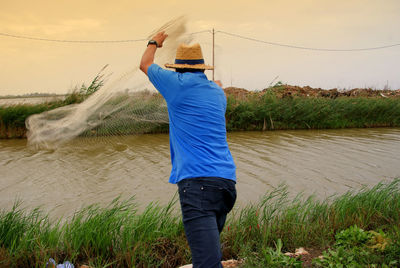 Rear view of man fishing in river against sky