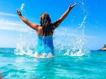 Woman splashing water in sea against blue sky