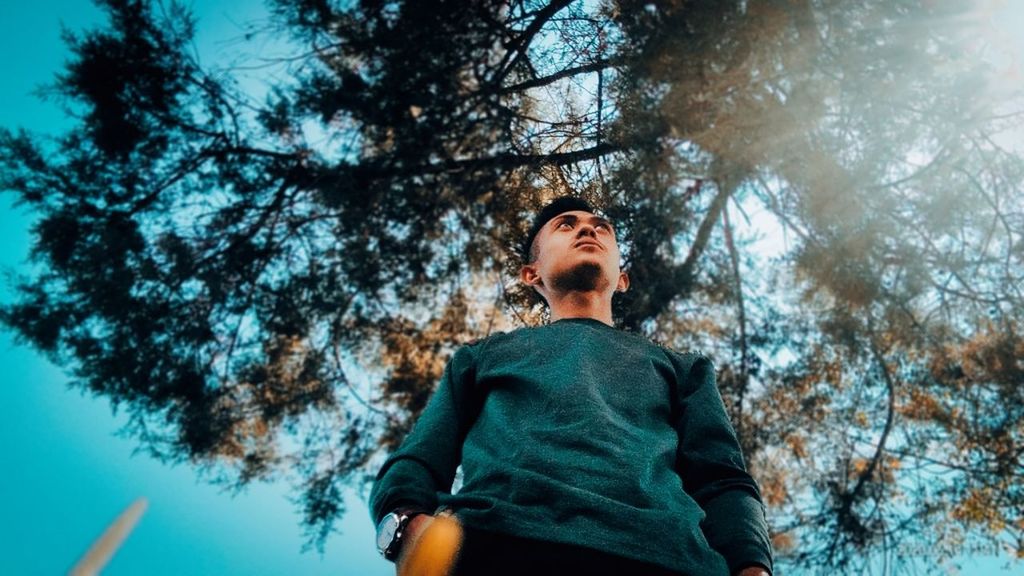 tree, plant, one person, nature, low angle view, spring, sunlight, young adult, adult, blue, leisure activity, looking up, sky, forest, clothing, waist up, lifestyles, looking, standing, day, outdoors, winter, land, casual clothing, women, three quarter length, beauty in nature, emotion, looking away, front view, men