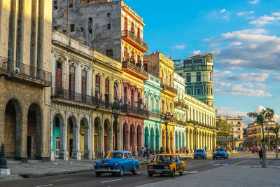 Cars on road by buildings in city against sky