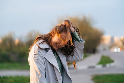 Beautiful smiling girl with long hair in a grey trench coat outdoors on the street spring