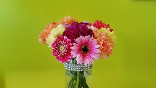 Close-up of colorful flowers in vase against green background