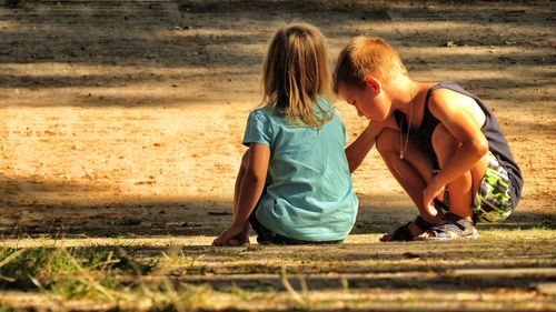 Friends crouching on grassy field during sunny day