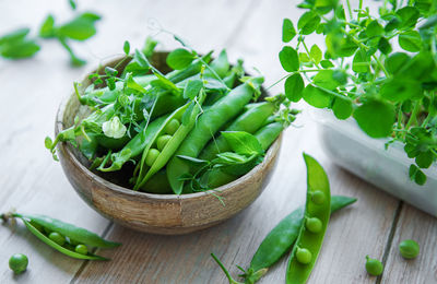 Bowl with young fresh juicy pods of green peas on a wooden background. healthy organic food.