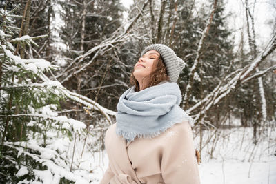 A cute girl stands under the snow with her eyes closed and smiles