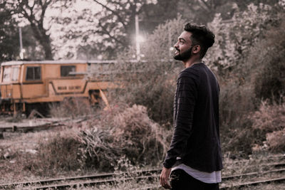 Side view of young man looking away against trees