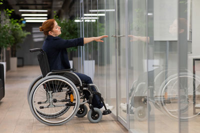 Red-haired caucasian woman in a wheelchair trying to open the door in the office