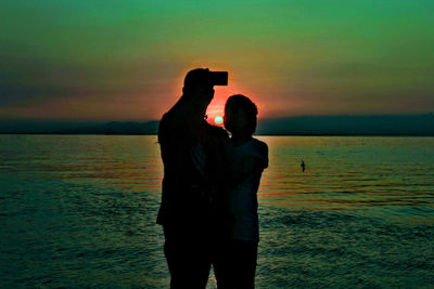 Silhouette couple standing on beach against sky during sunset