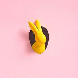 Yellow easter bunny looks out of an egg-shaped hole in the pink background wall. abstract concept. 