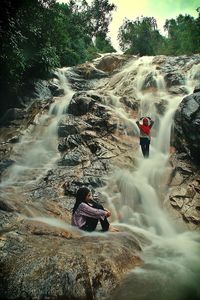 People sitting on rock in waterfall