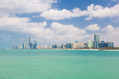 Sea by modern buildings against sky in city