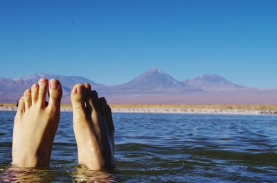 Low section of person in sea against clear blue sky