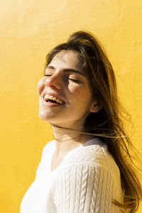 Woman with eyes closed laughing in front of yellow wall