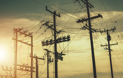 Low angle view of electricity pylon against sky during sunset