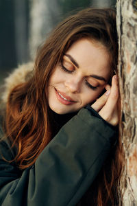 Portrait of smiling young woman against tree trunk