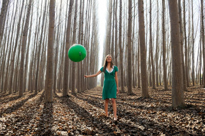 Full length of woman holding balloon while standing in forest
