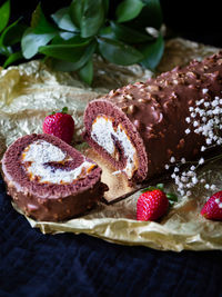 Rolled chocolate cake with white cream inside. red strawberries golden and dark blue background