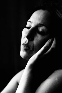 Close-up of woman with closed eyes sitting against black background