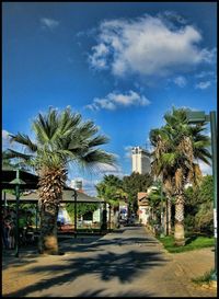 Road leading towards palm trees against blue sky