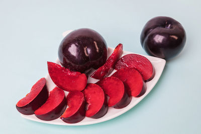 On a white saucer there is a large plum cut into wedges, next to it there are two more plums.