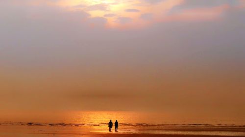 Silhouette people on beach against sky during sunset